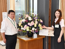 市役所の新本庁舎エントランスに飾られた花と、藤森部長（写真左）ら