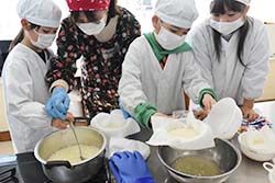 出来上がった豆腐をザルに入れ水気を切る作業をすすめる児童