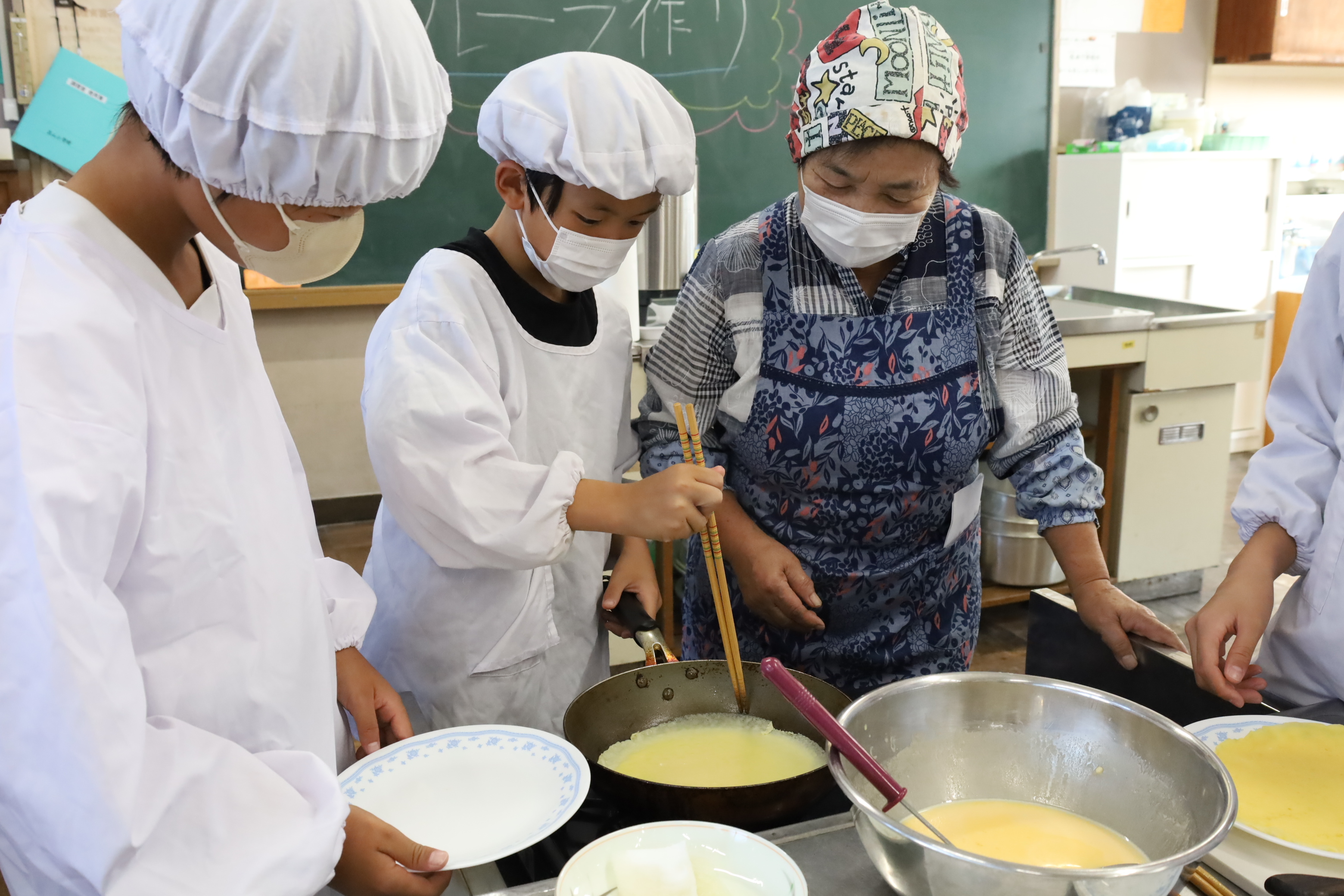 メンバーの優しい指導で生地を焼く児童