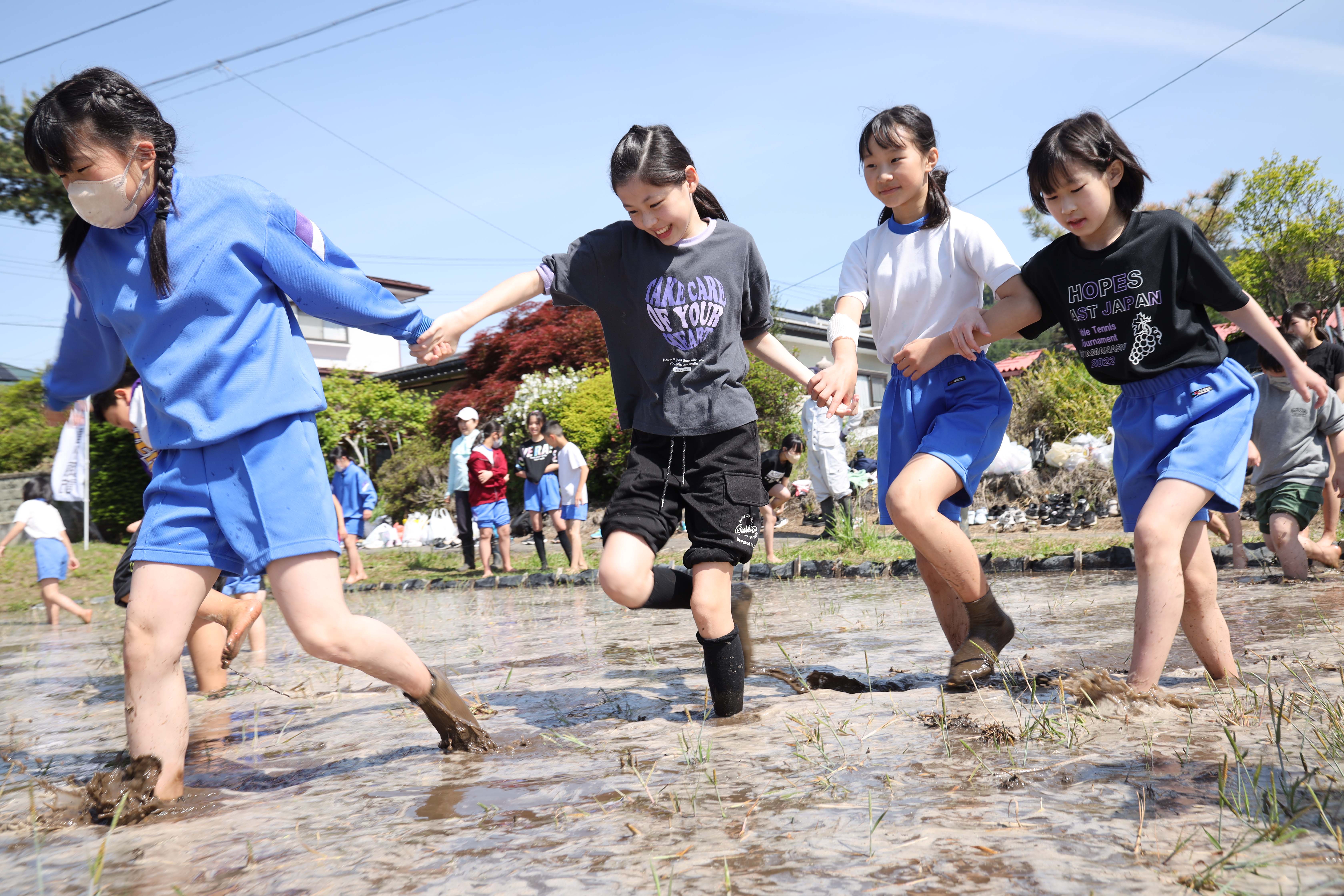 田んぼの中で、土や水と目いっぱいに触れ合う児童（長野県岡谷市で）